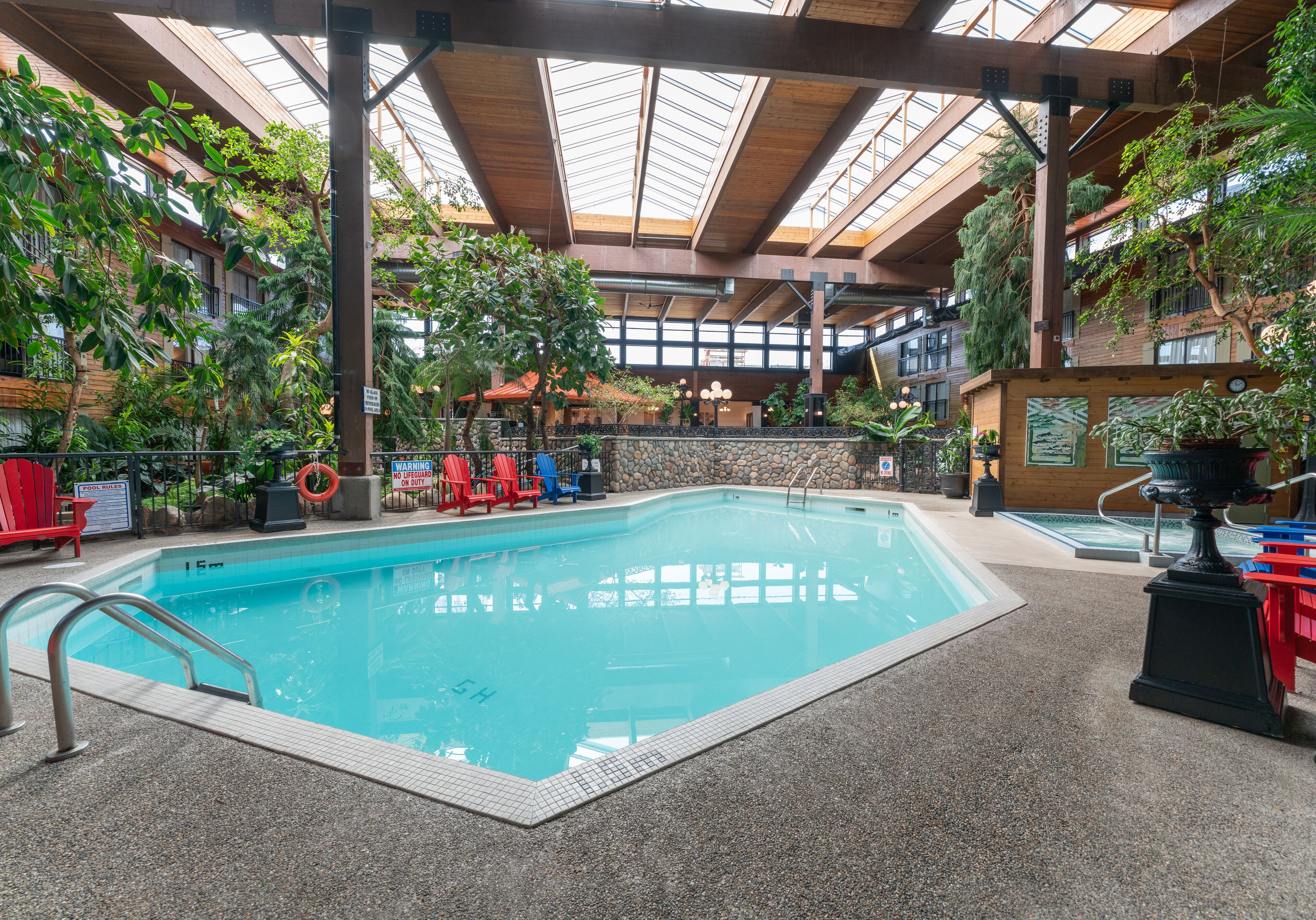 An indoor swimming pool with a stone wall, surrounded by potted plants and red chairs.