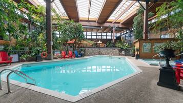 An indoor swimming pool with a stone wall, surrounded by potted plants and red chairs.
