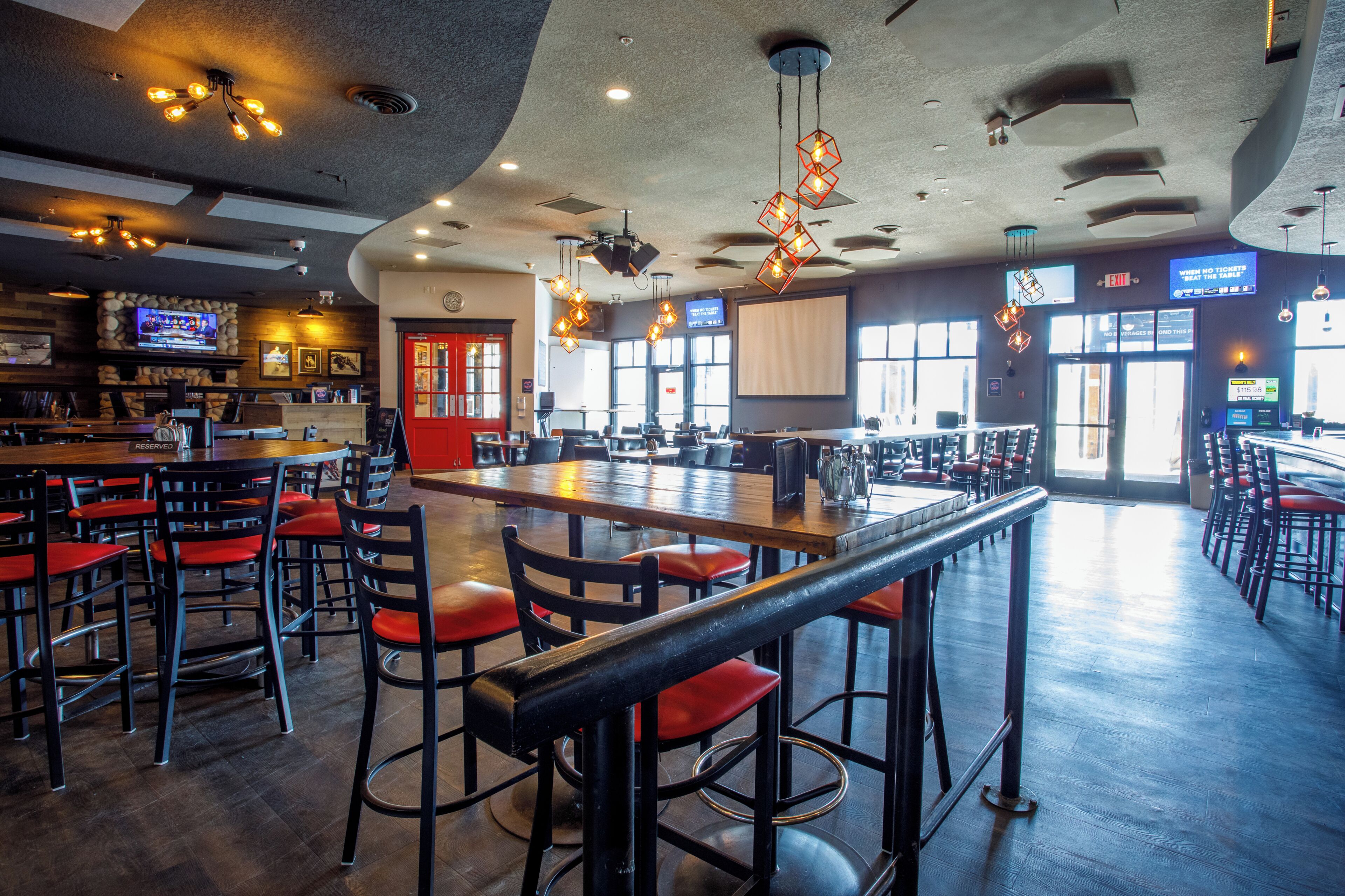 A restaurant with high tables, red cushioned chairs, and a bar area.