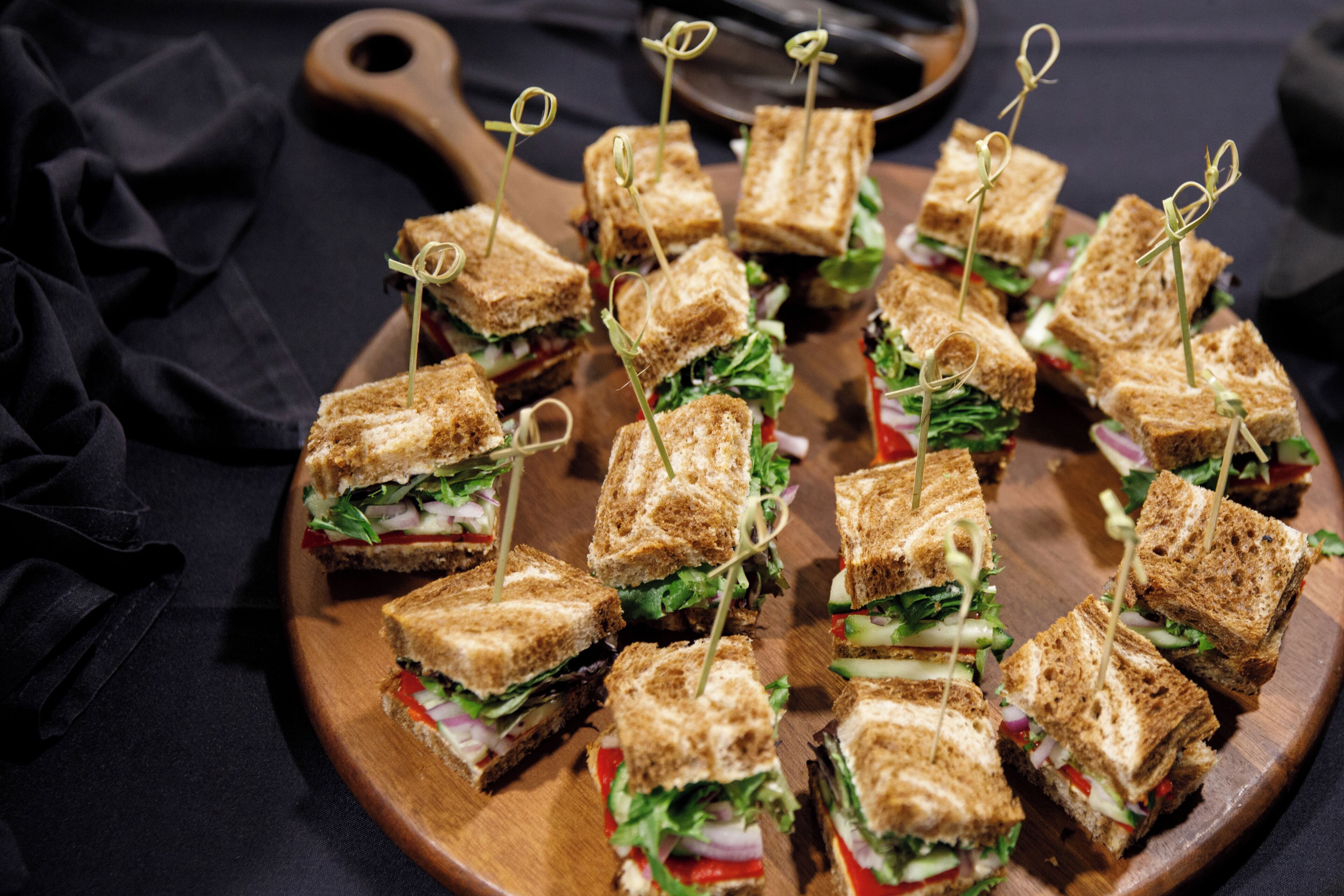 Una tabla de madera con varios sándwiches, cada uno sujeto con palillos.