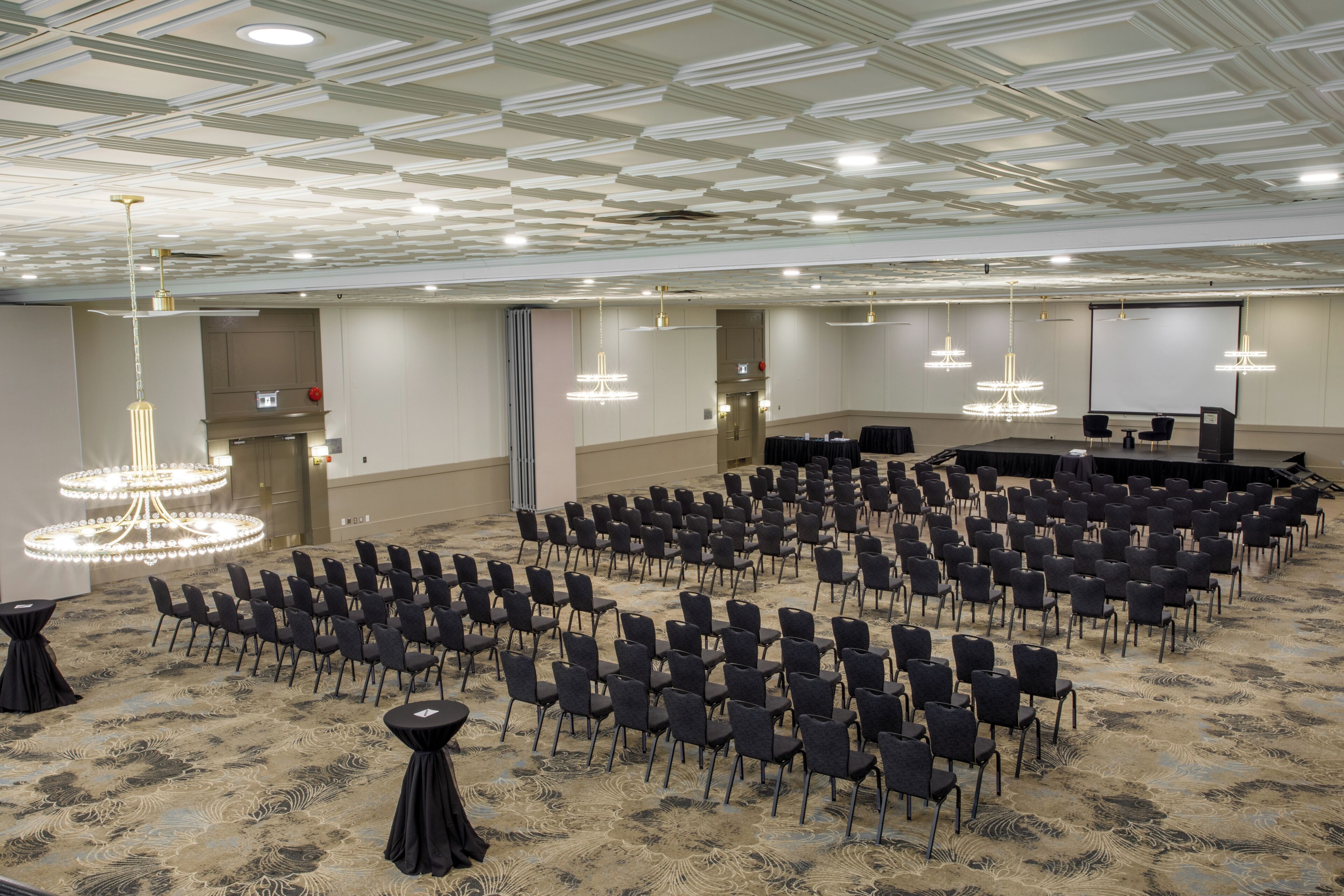 A conference room with rows of chairs, a stage, and a large screen.