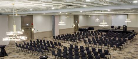A conference room with rows of chairs, a stage, and a large screen.