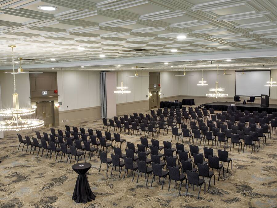 A conference room with rows of chairs, a stage, and a large screen.