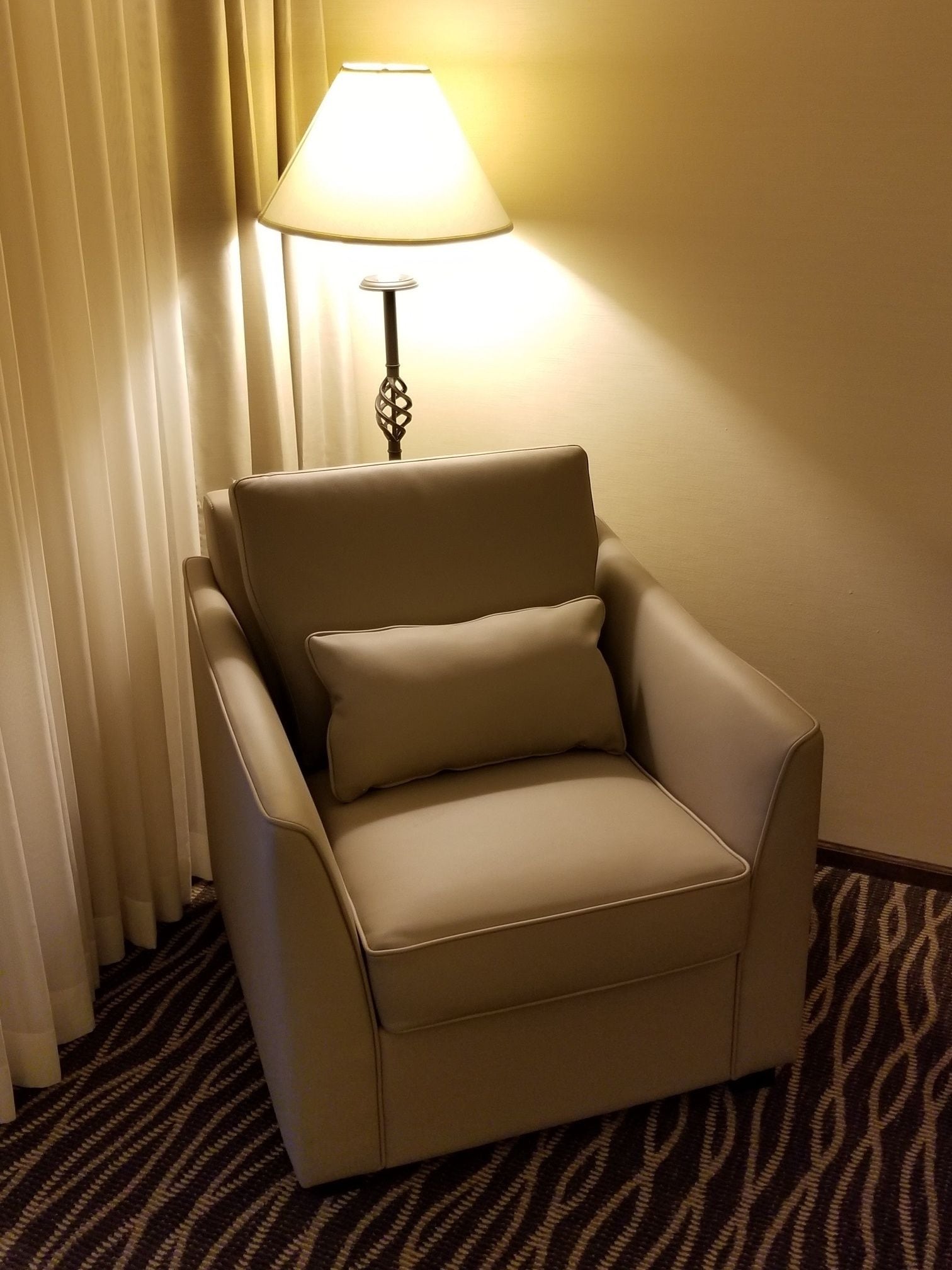 A beige armchair with a matching pillow, positioned next to a lamp with a white shade.