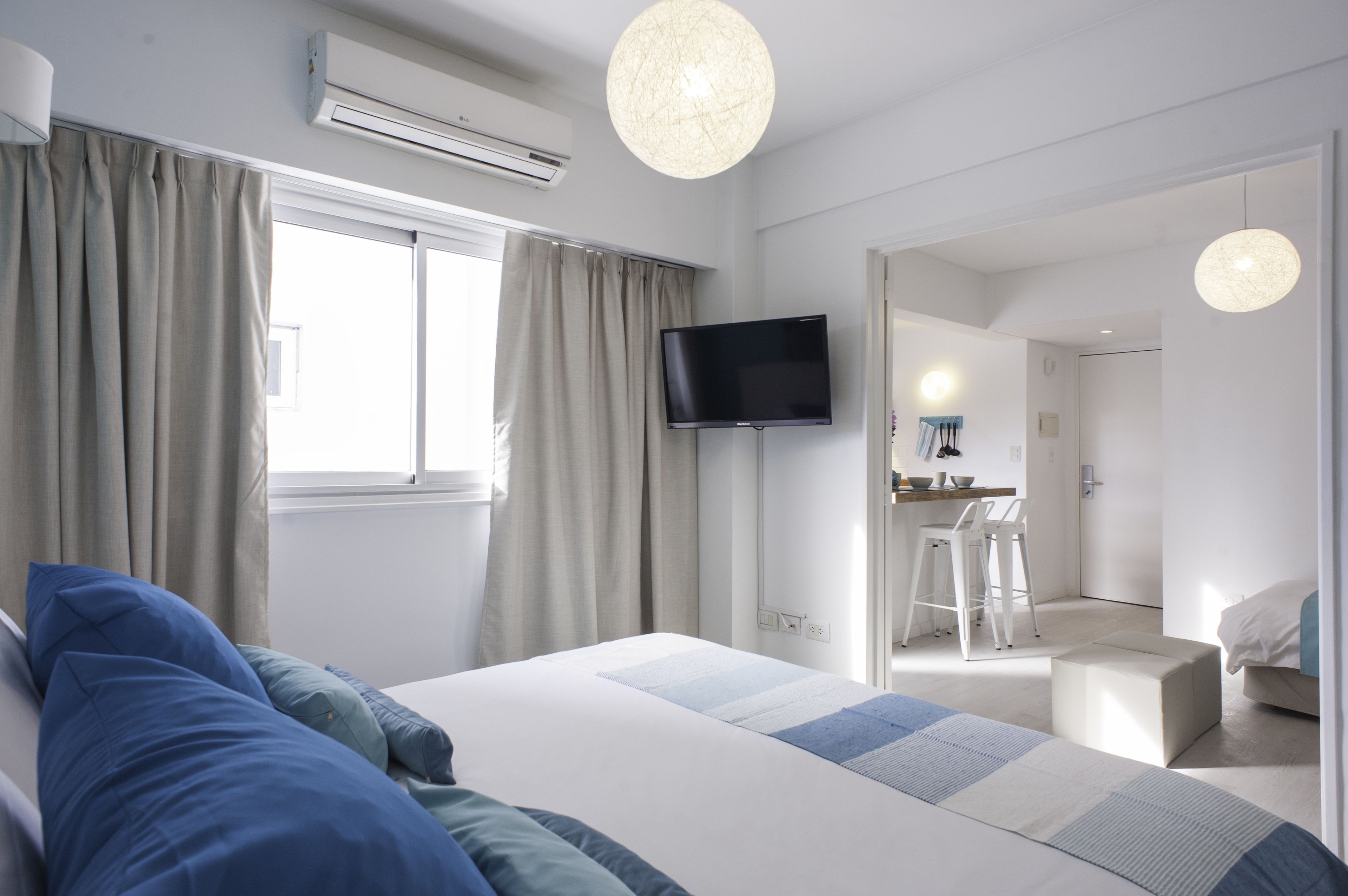 A modern hotel room with a bed, a flat-screen TV, a desk with a chair, and a large window with curtains.