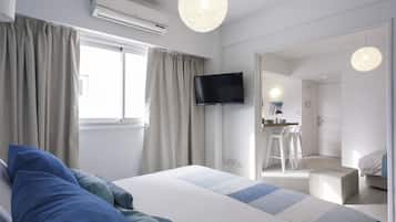 A modern hotel room with a bed, a flat-screen TV, a desk with a chair, and a large window with curtains.