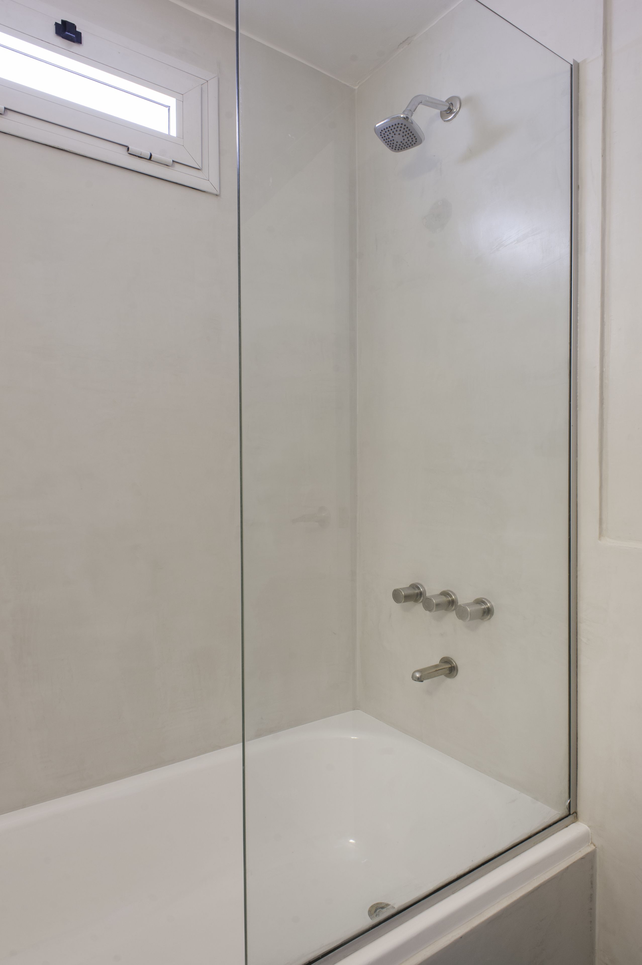 A glass-enclosed shower stall with a handheld showerhead and a wall-mounted control panel.