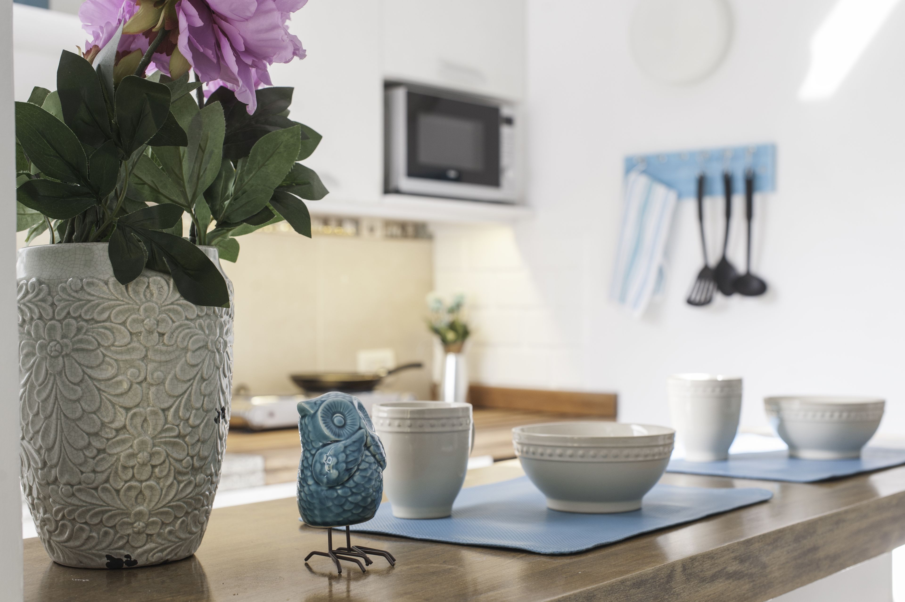 A kitchen with a decorative vase, a blue owl figurine, and white bowls on a counter.