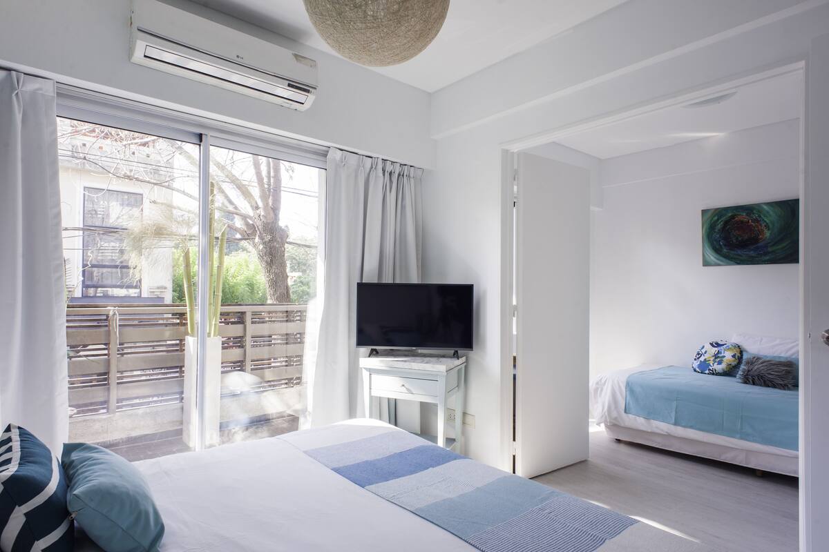 A bedroom with a large bed, a TV on a small table, and a balcony with a view of the outside.