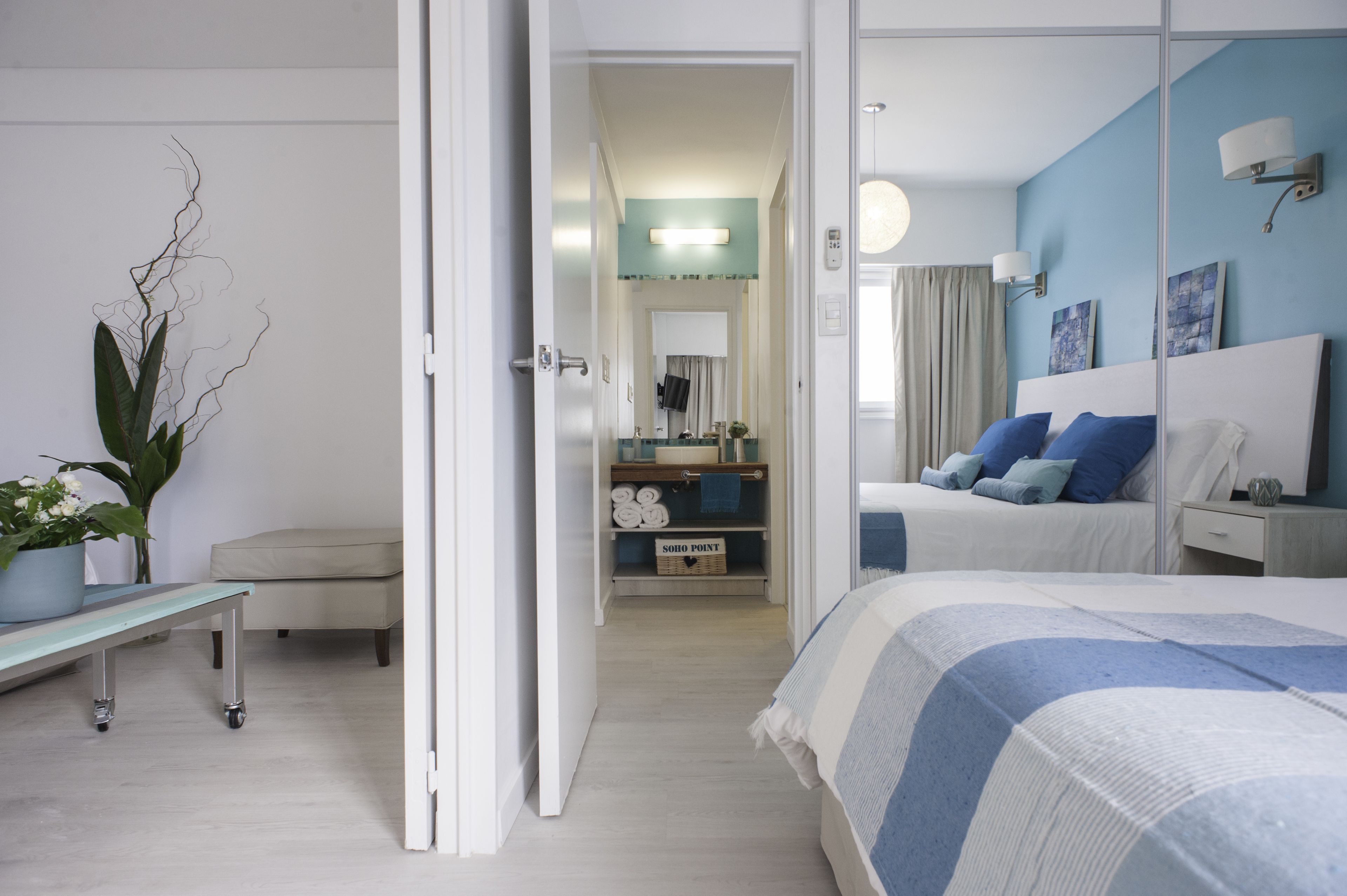A modern hotel room with a large bed, a bedside table, a potted plant, and a view of the hallway.