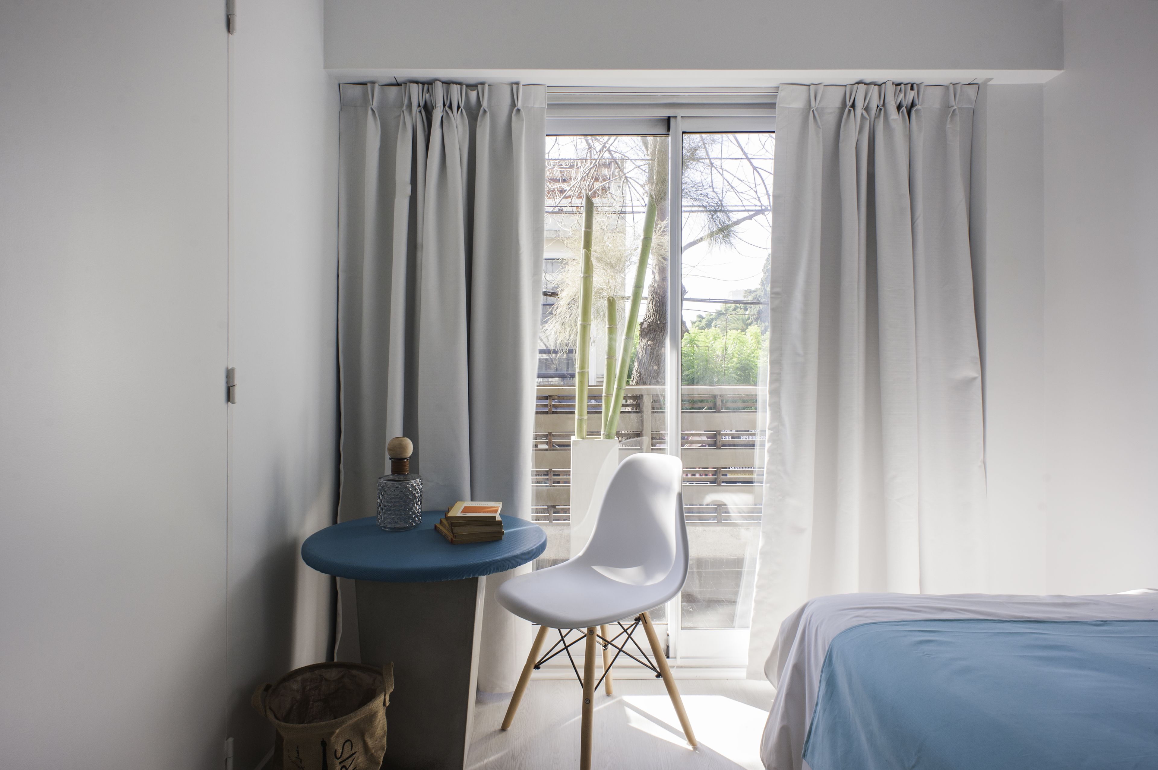 A room with a bed, a small table with a chair, and a window with curtains.