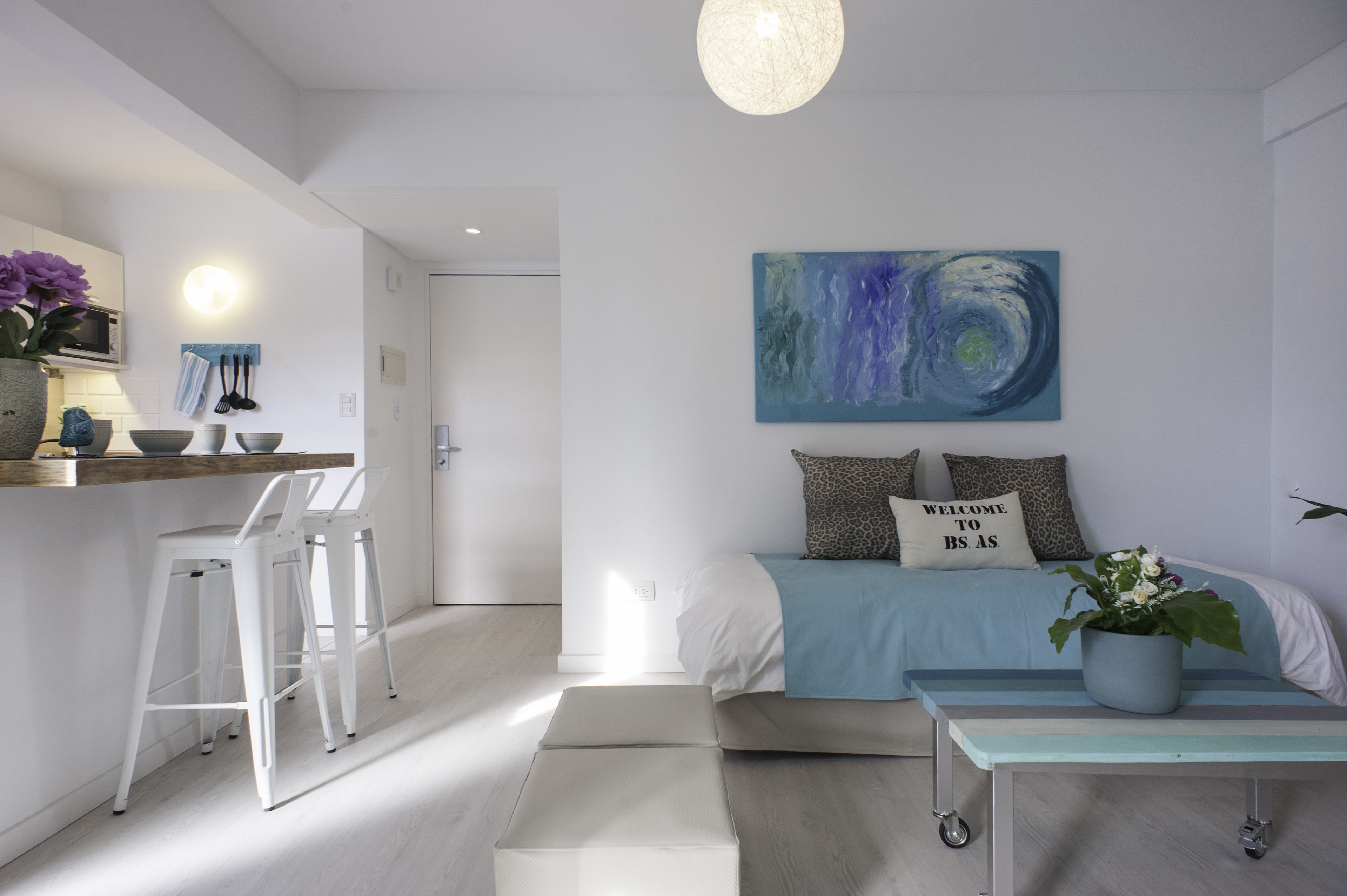 Une chambre à coucher moderne et minimaliste, avec un lit, un tableau abstrait bleu et un panneau d’accueil.