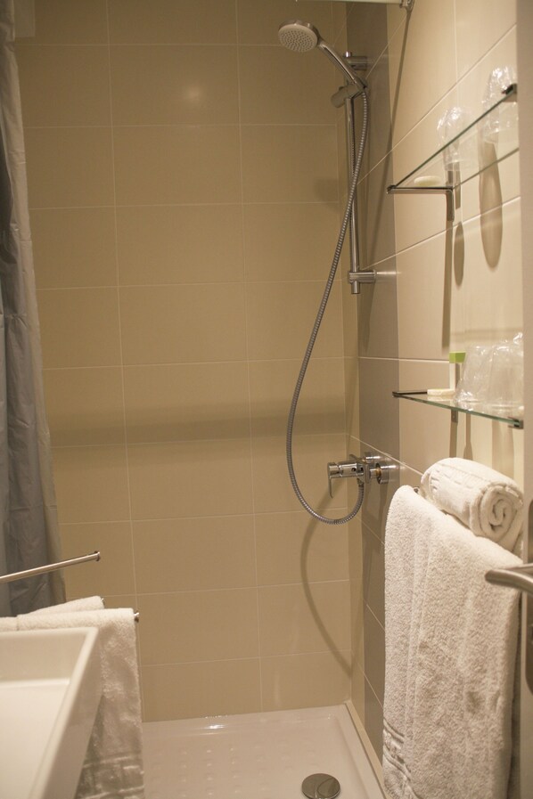 A shower area with a glass shelf holding toiletries, a showerhead, and a towel rack with towels. - Hotel Le Concorde (Aix-en-Provence)