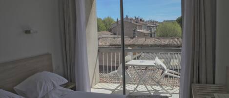 A hotel room with a bed, a small table, and a balcony with chairs.