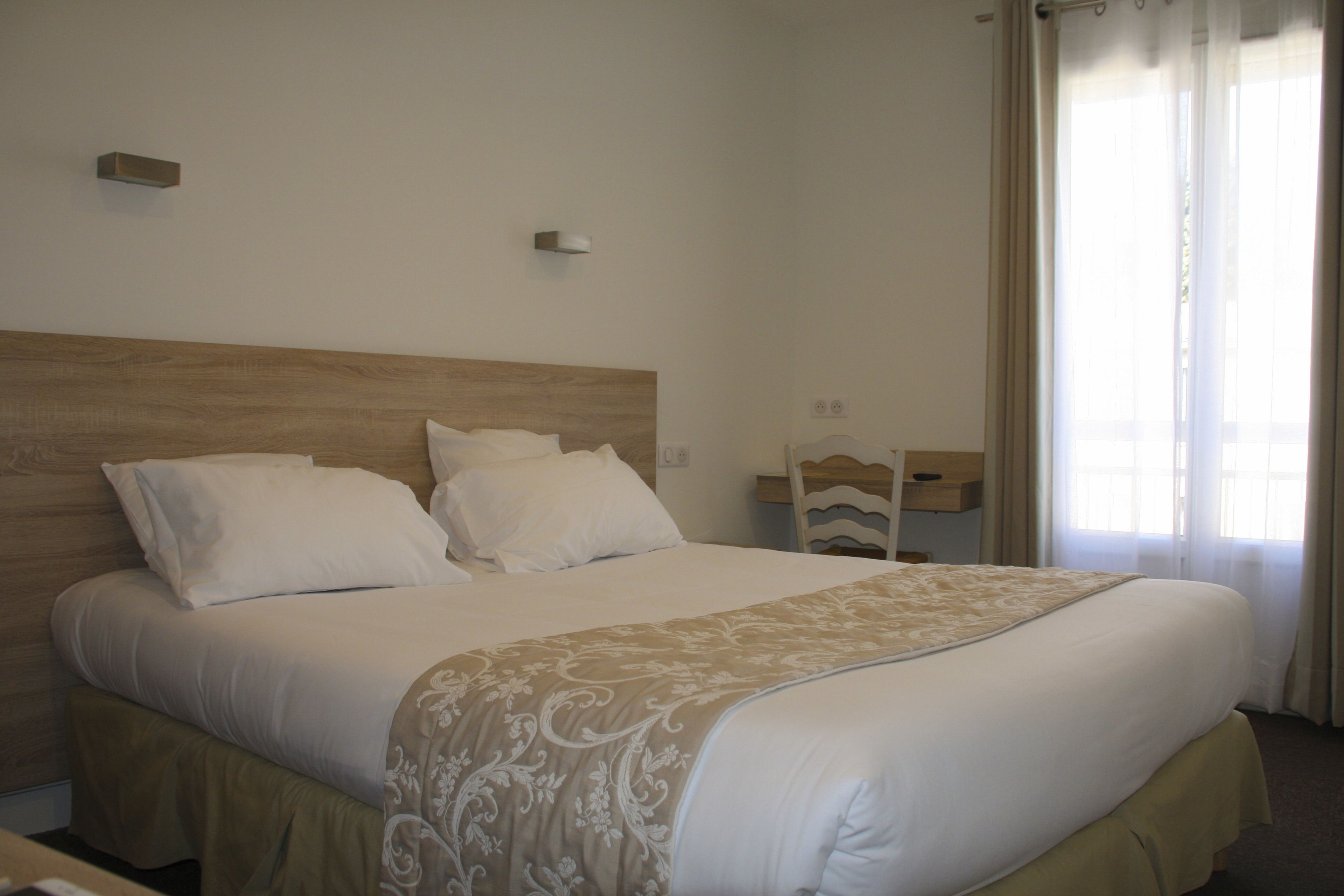 A neatly made bed with a wooden headboard, a bedside table with a lamp, and a window with curtains.