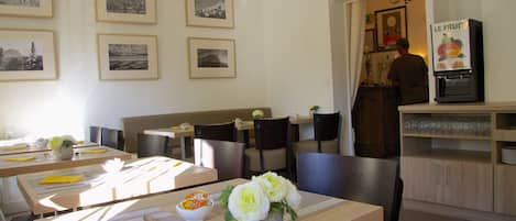 Un restaurante con mesas dispuestas para comer, cuadros en la pared y un refrigerador con una exhibición de frutas.