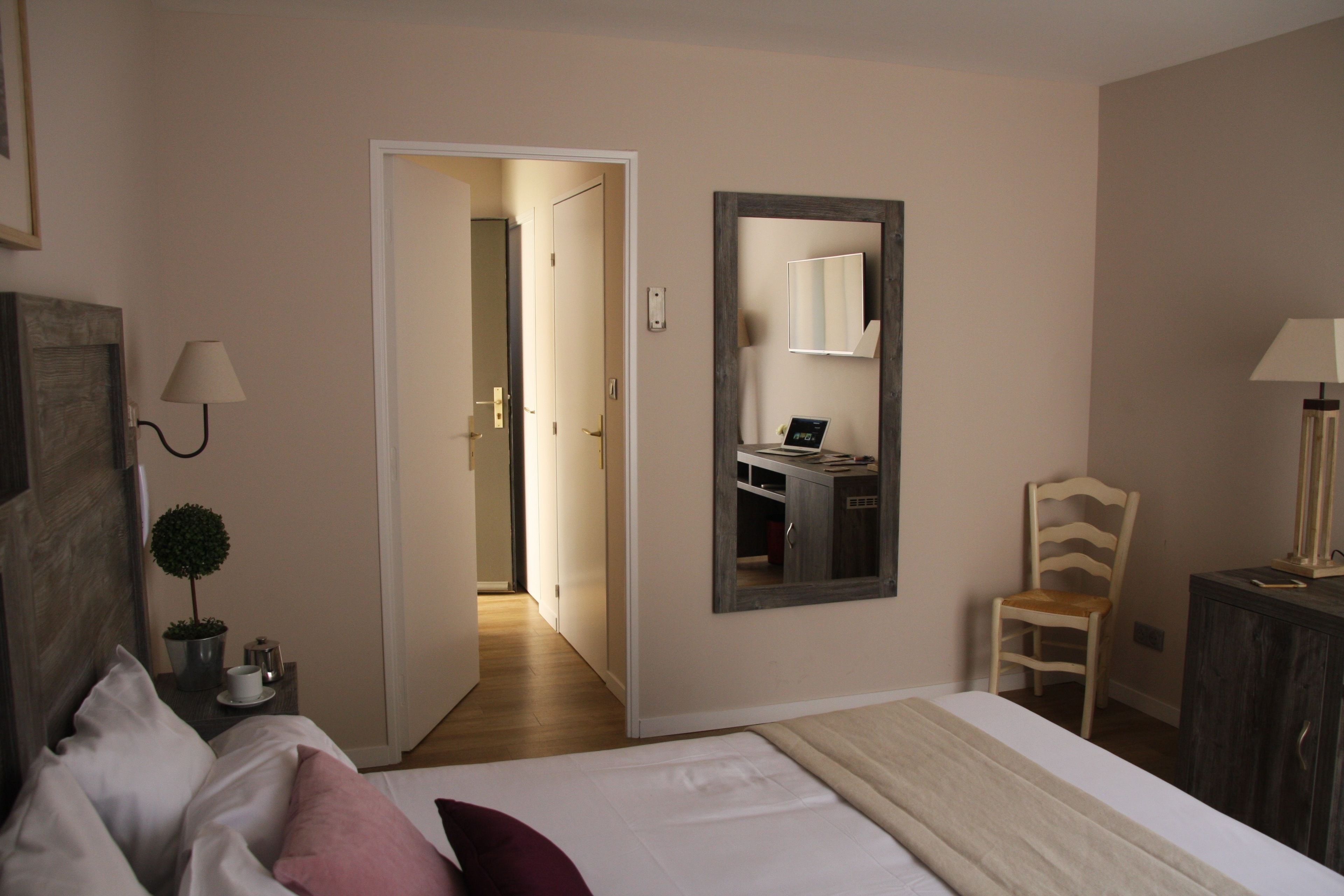 A hotel room with a bed, a chair, a desk with a computer, a mirror, and a lamp.
