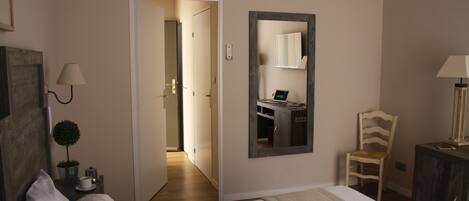 A hotel room with a bed, a chair, a desk with a computer, a mirror, and a lamp.