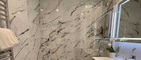 A modern bathroom with a marble wall, a bathtub, a wooden vanity, and a large mirror.