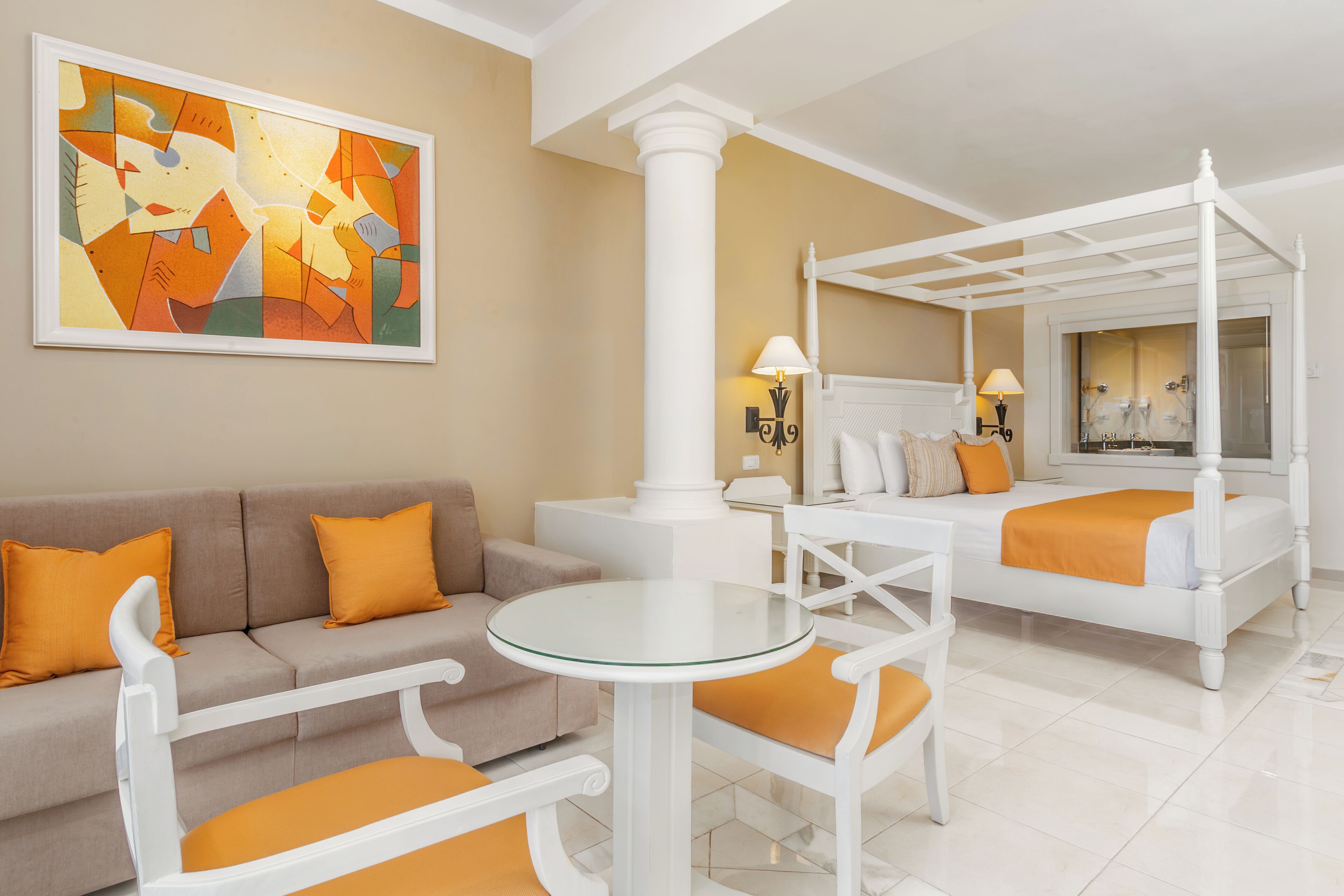A hotel room with a bed, a sofa, a glass table, and a painting on the wall.