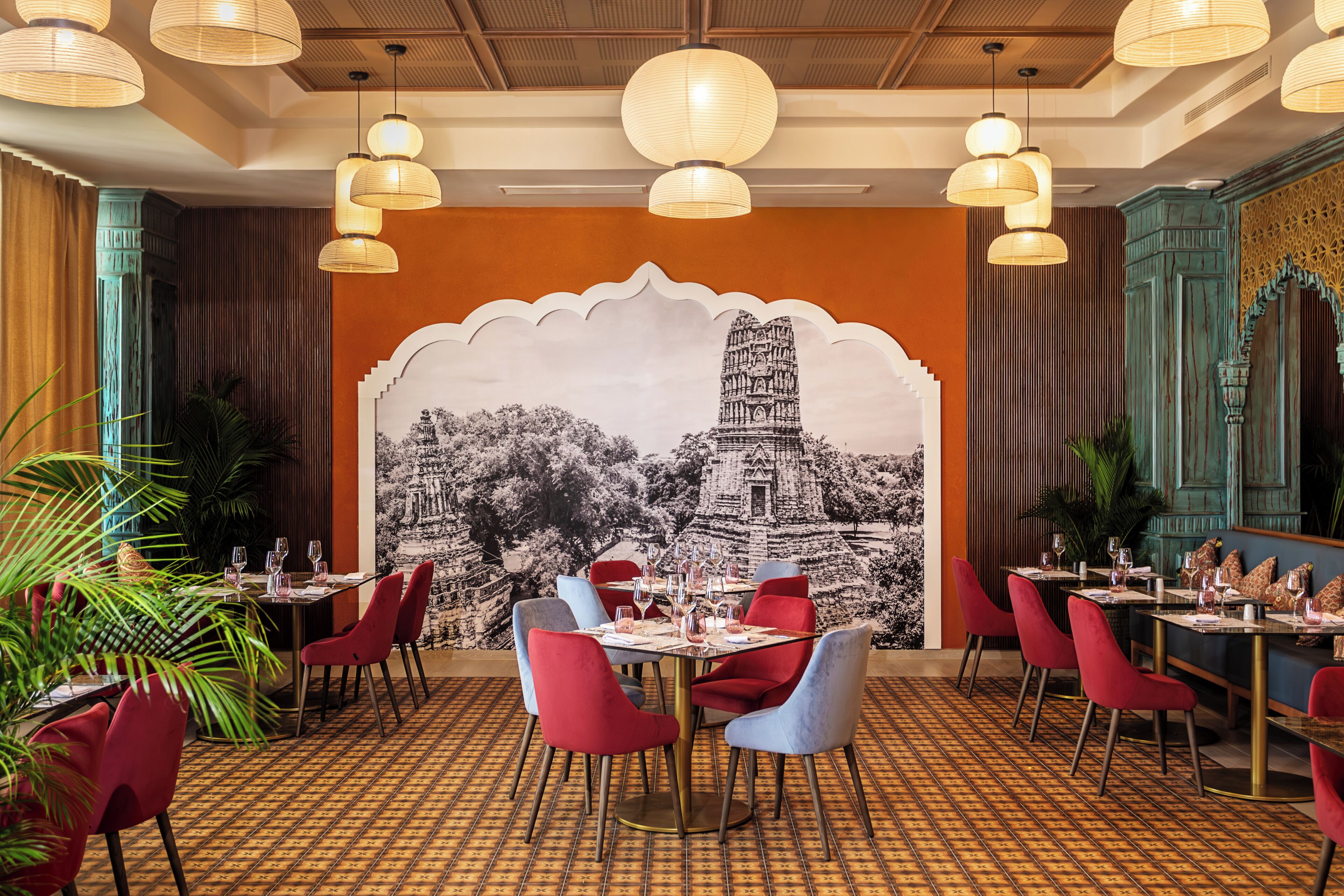 A restaurant with a mural of a temple, red and blue chairs, and hanging paper lanterns.