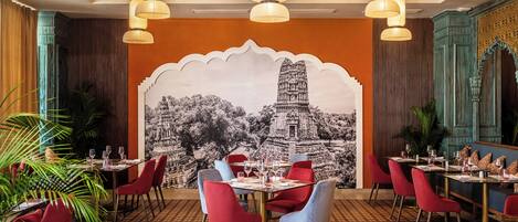 A restaurant with a mural of a temple, red and blue chairs, and hanging paper lanterns.