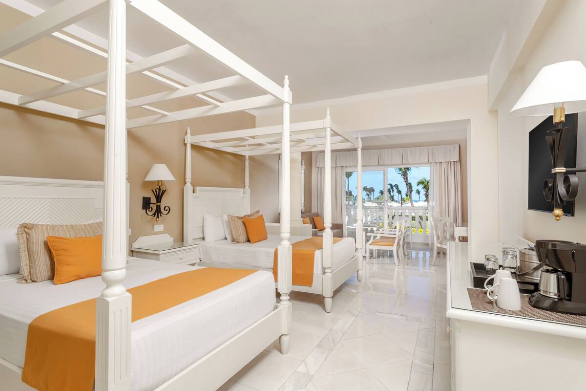 A hotel room with a four-poster bed, a separate bedroom, a balcony with a view, and a coffee station.