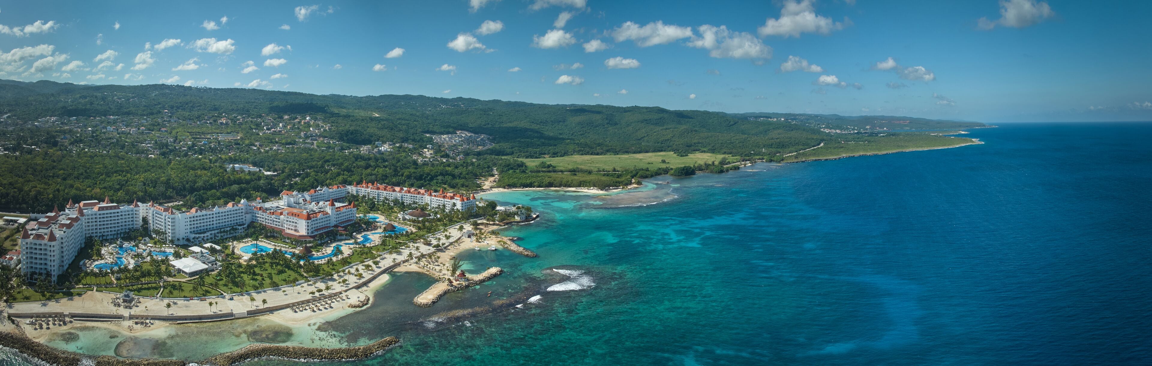 Un complejo turístico con varias construcciones, una playa y aguas azules cristalinas.