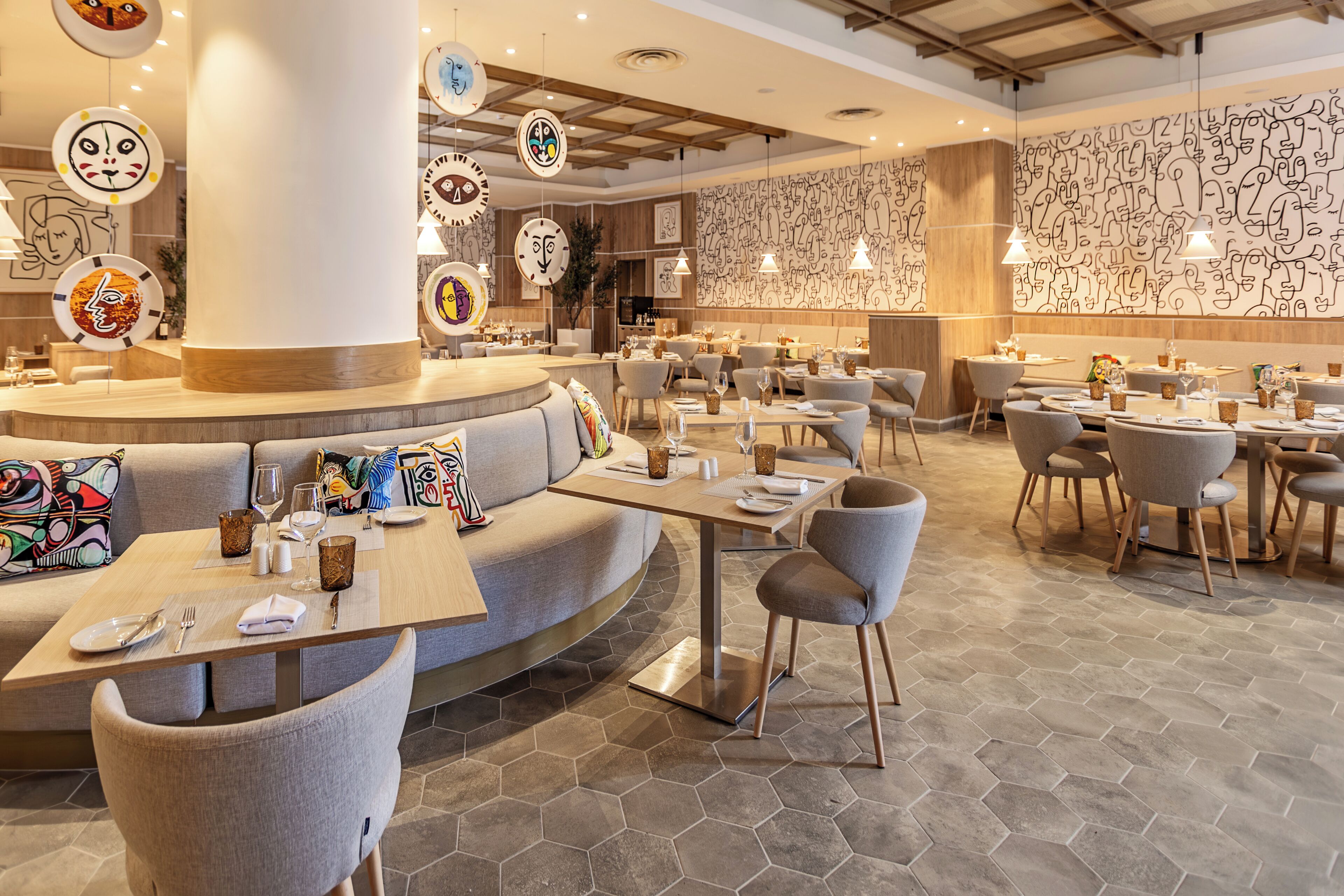 En moderne restaurant med runde borde, polstrede siddepladser og et unikt vægkunstdesign.