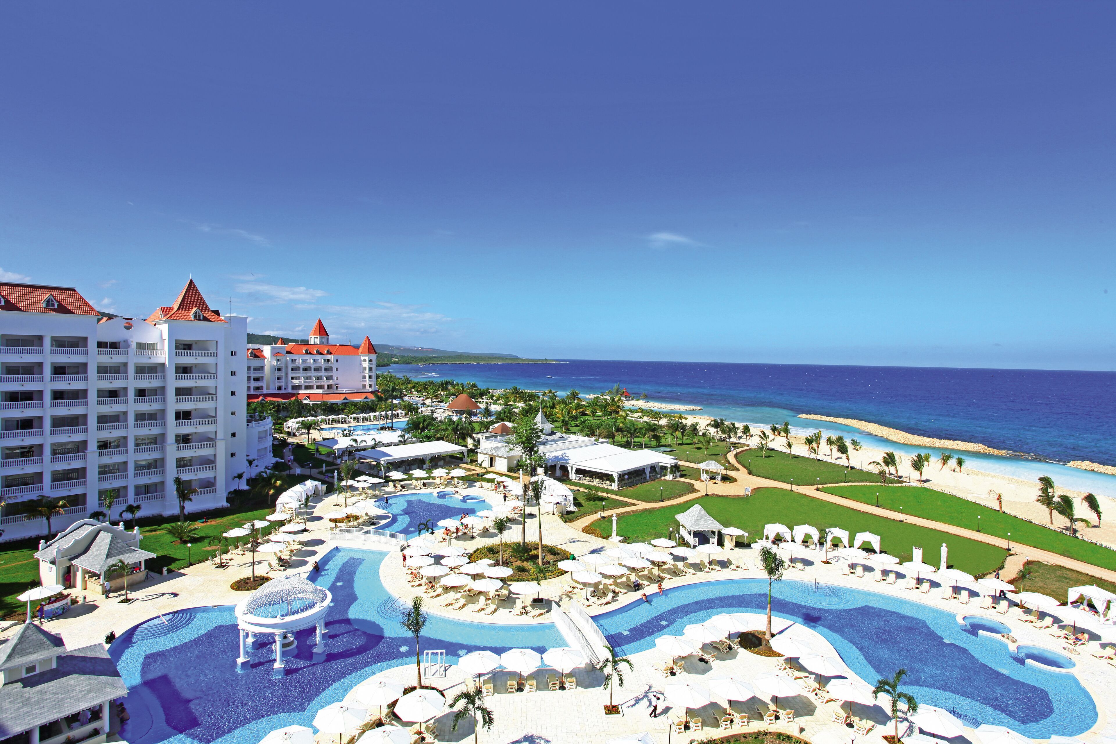 A resort with a large swimming pool, beach, and hotel buildings.