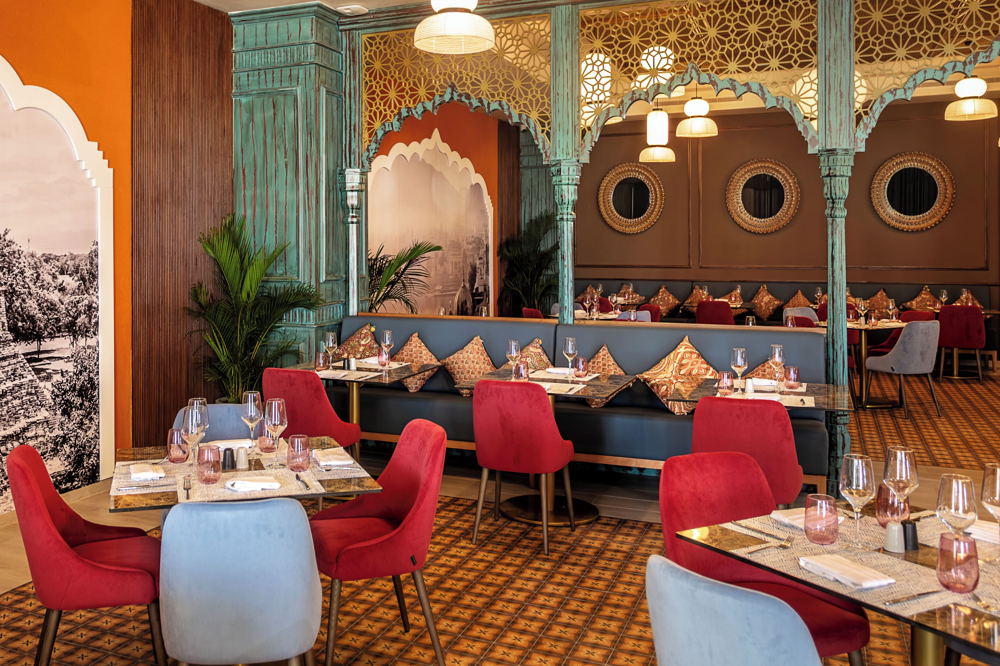 A restaurant with red and blue chairs, tables set with wine glasses, and a patterned floor.