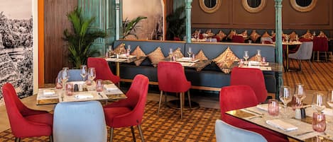 Un restaurante con sillas rojas y azules, mesas preparadas con copas de vino y un suelo estampado.
