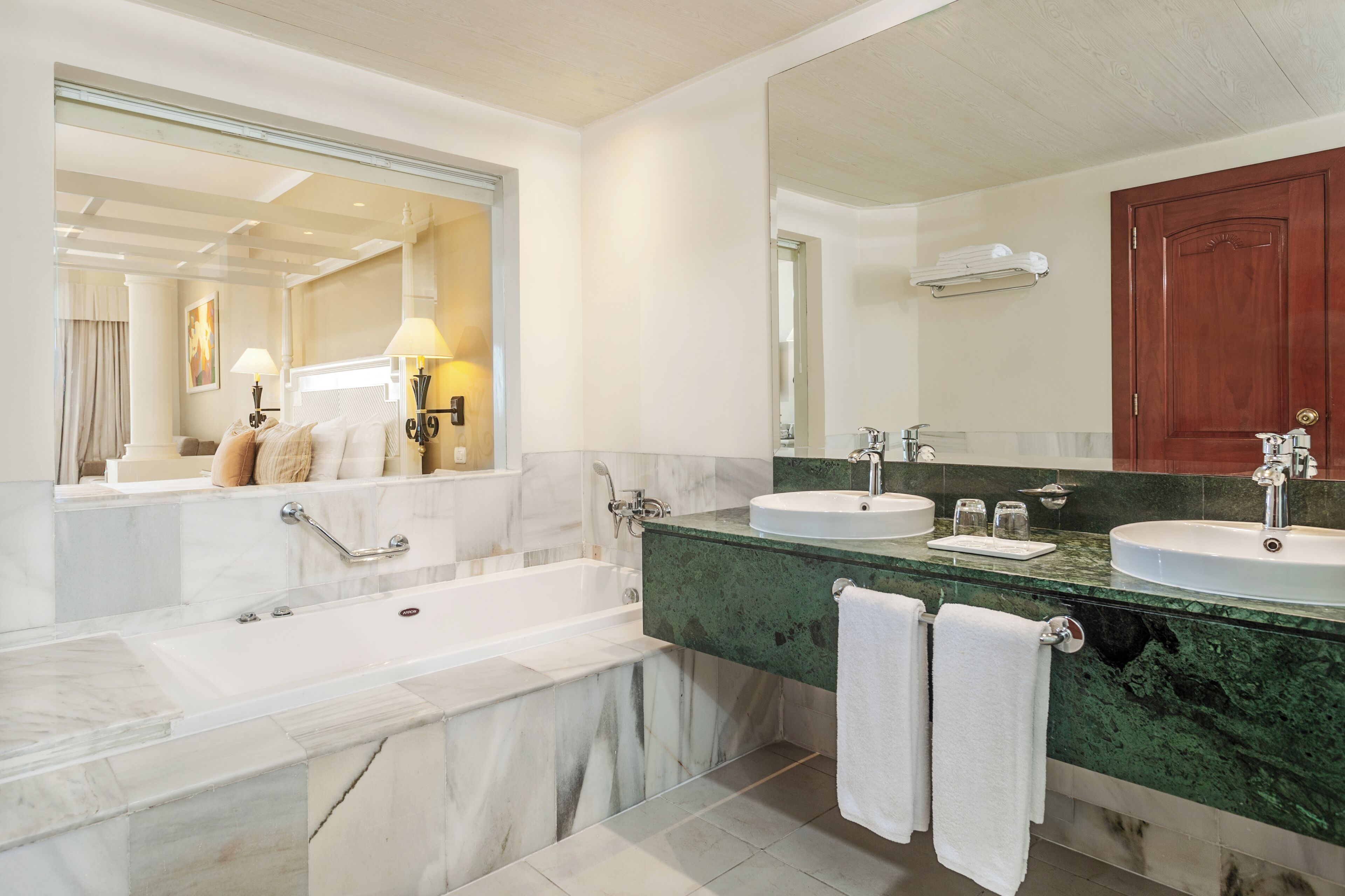 A modern bathroom with a large mirror, two sinks, a bathtub, and a towel rack.