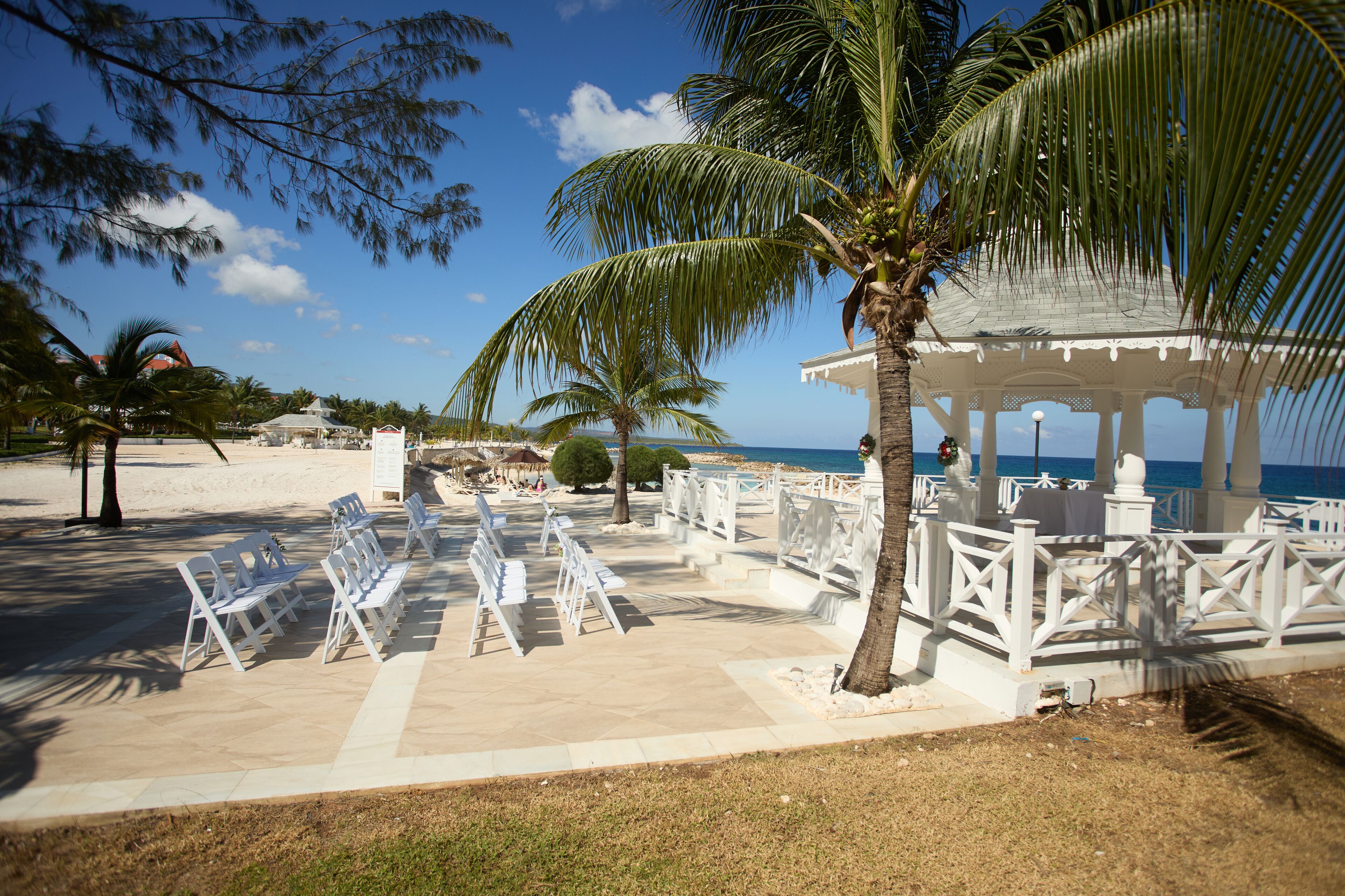 A beachside gazebo with white railings and a palm tree in the foreground.