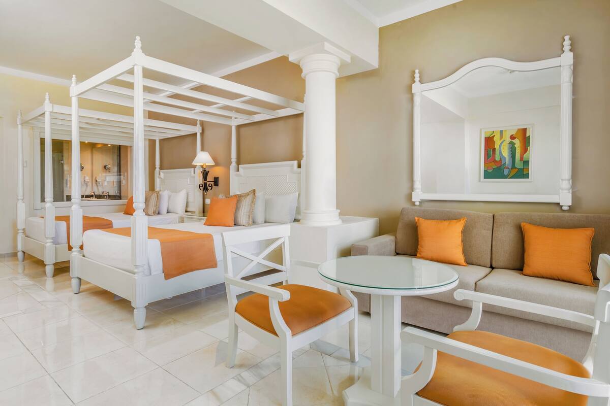 A hotel room with a four-poster bed, a sofa, a glass coffee table, and a large mirror.