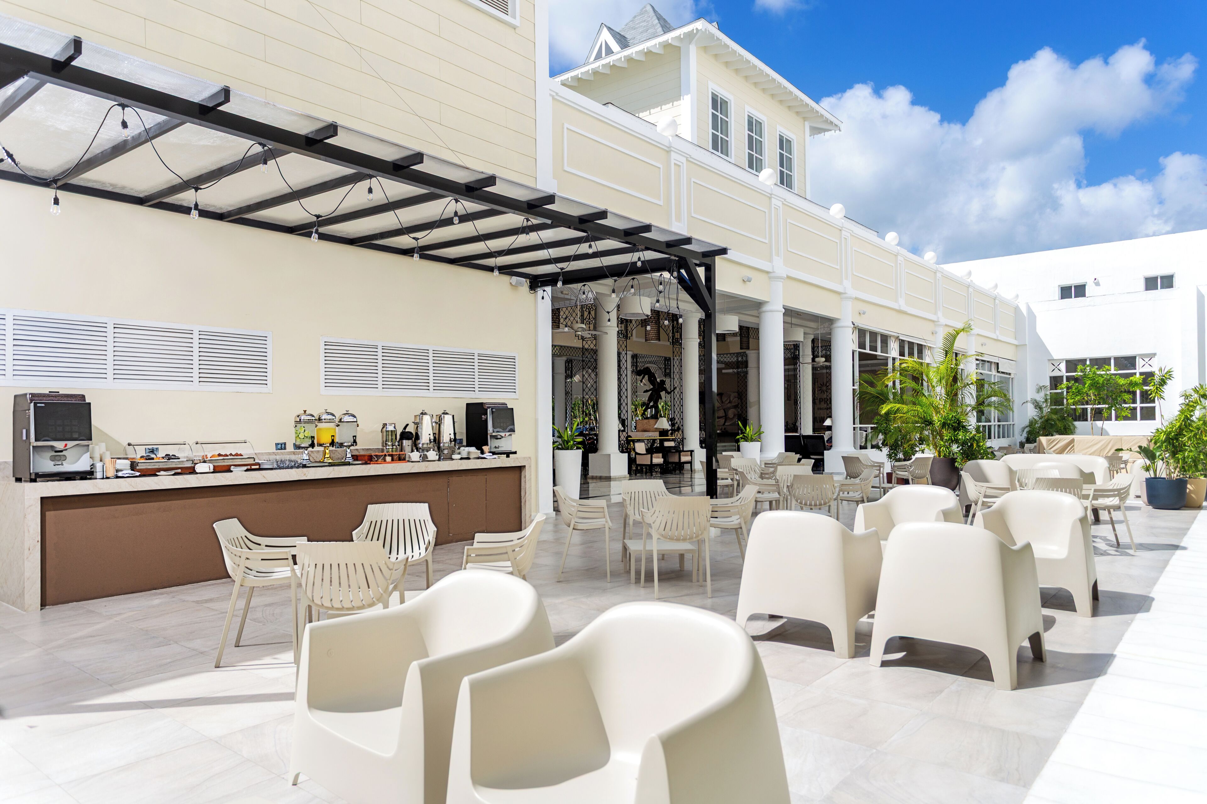 Une terrasse extérieure avec des chaises blanches, un espace bar et un coin salon abrité.