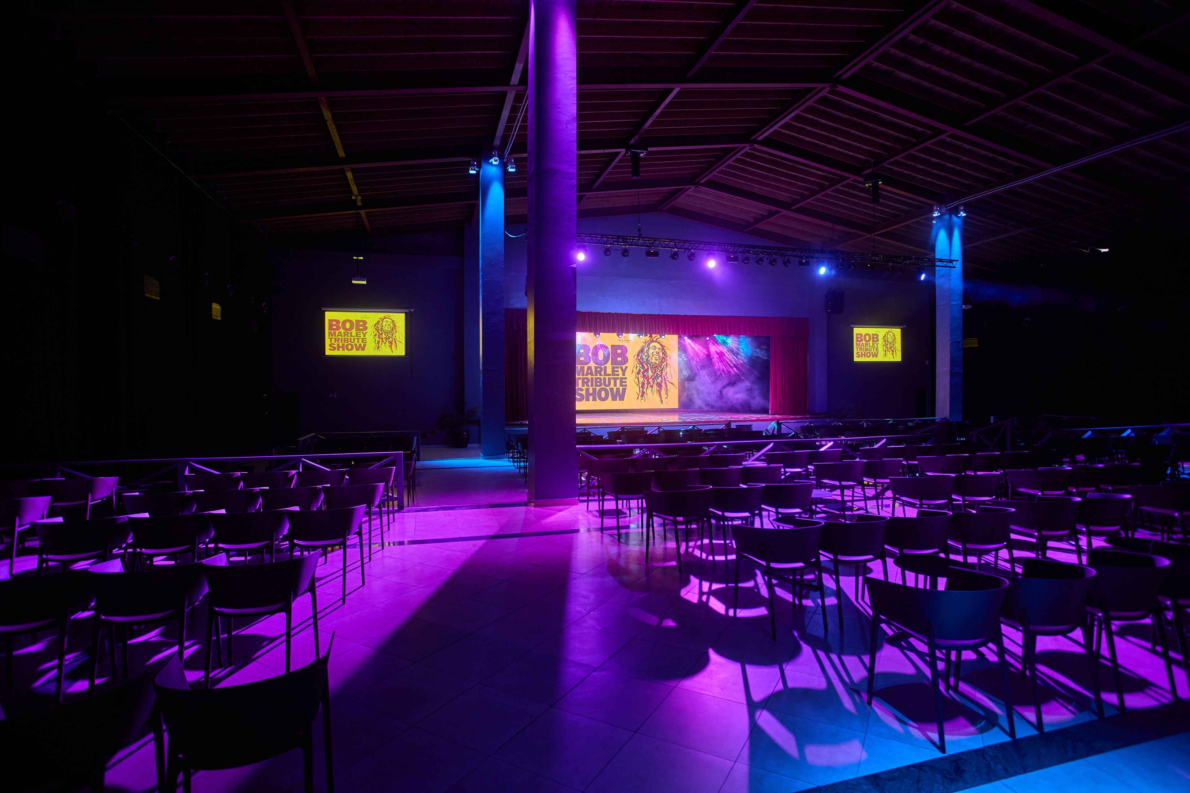 Een auditorium met rijen stoelen, een podium met een groot scherm en een spandoek met de tekst 