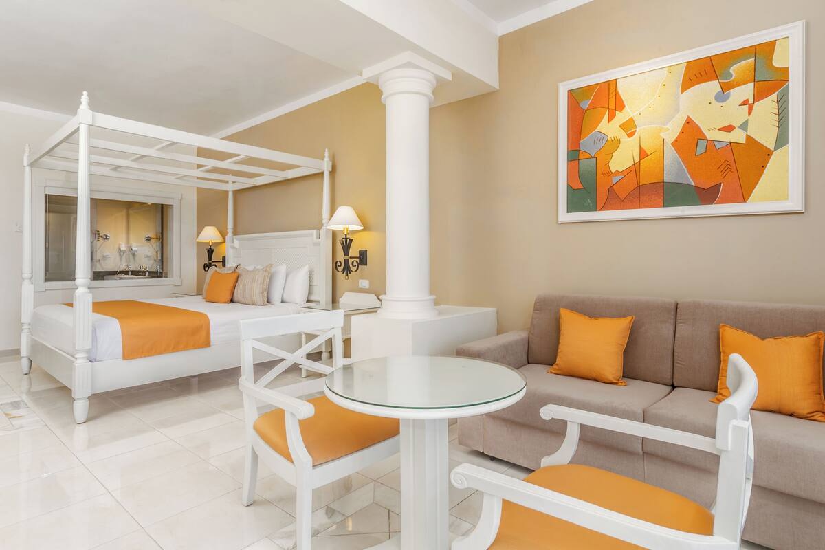 A hotel room with a bed, a sofa, a round table, and a painting on the wall.