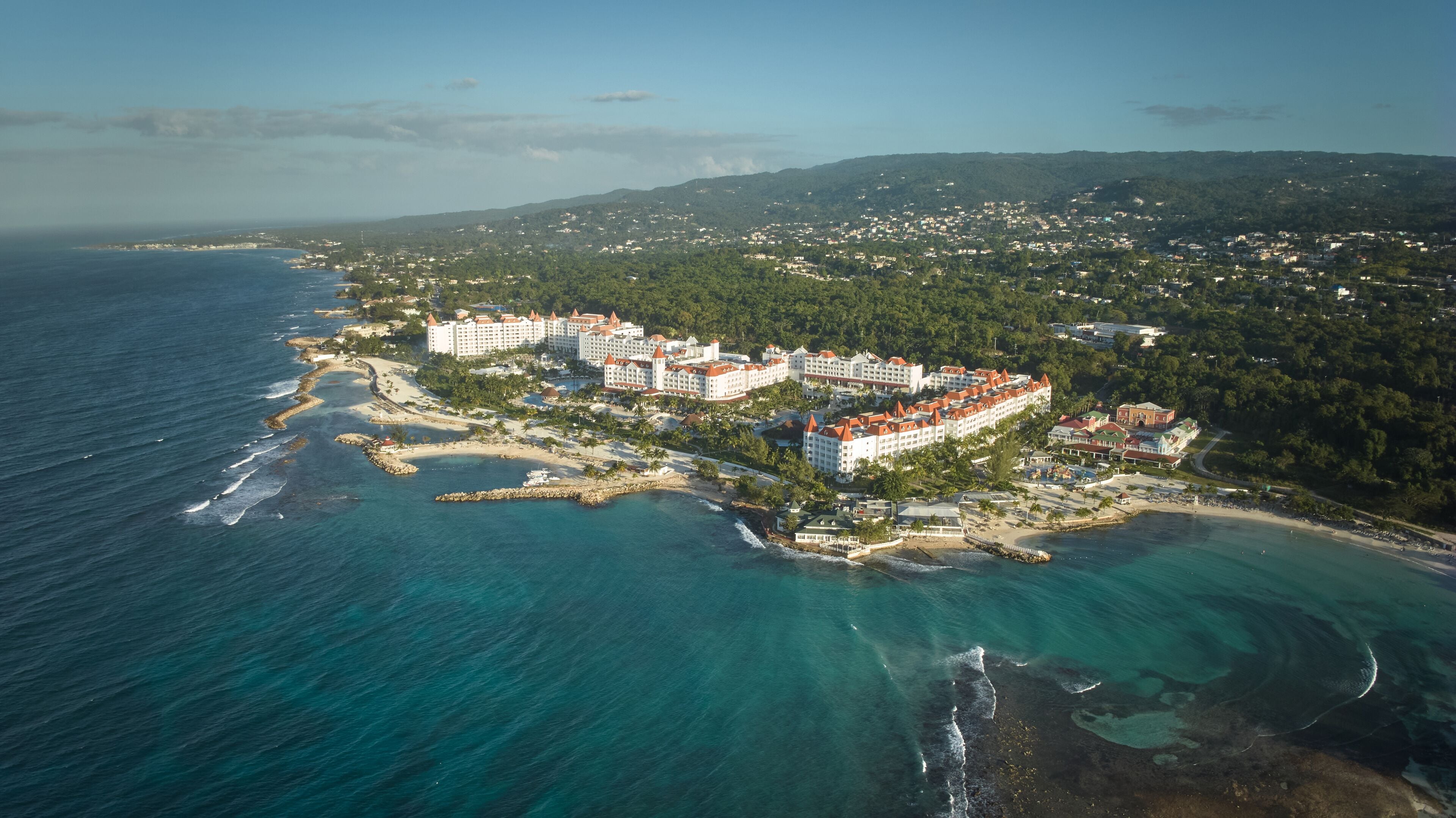 Vista aérea de un complejo turístico costero con varios edificios de hotel, acceso directo a la playa y vegetación circundante.