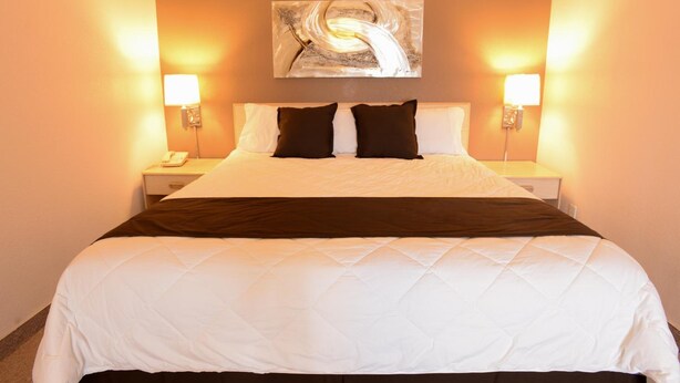 A hotel room with a large bed, two bedside tables, and a wall-mounted abstract painting. - Burlington Inn (Burlington)
