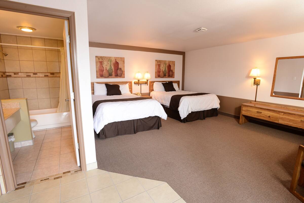 A hotel room with two beds, a bathroom, and a wooden bench.