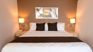 A hotel room with a large bed, two bedside lamps, a wall-mounted abstract painting, and a telephone on the nightstand. - Burlington Inn (Burlington)