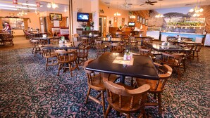 A restaurant with wooden tables and chairs, a patterned carpet, ceiling fans, and a television on the wall. - Burlington Inn (Burlington)