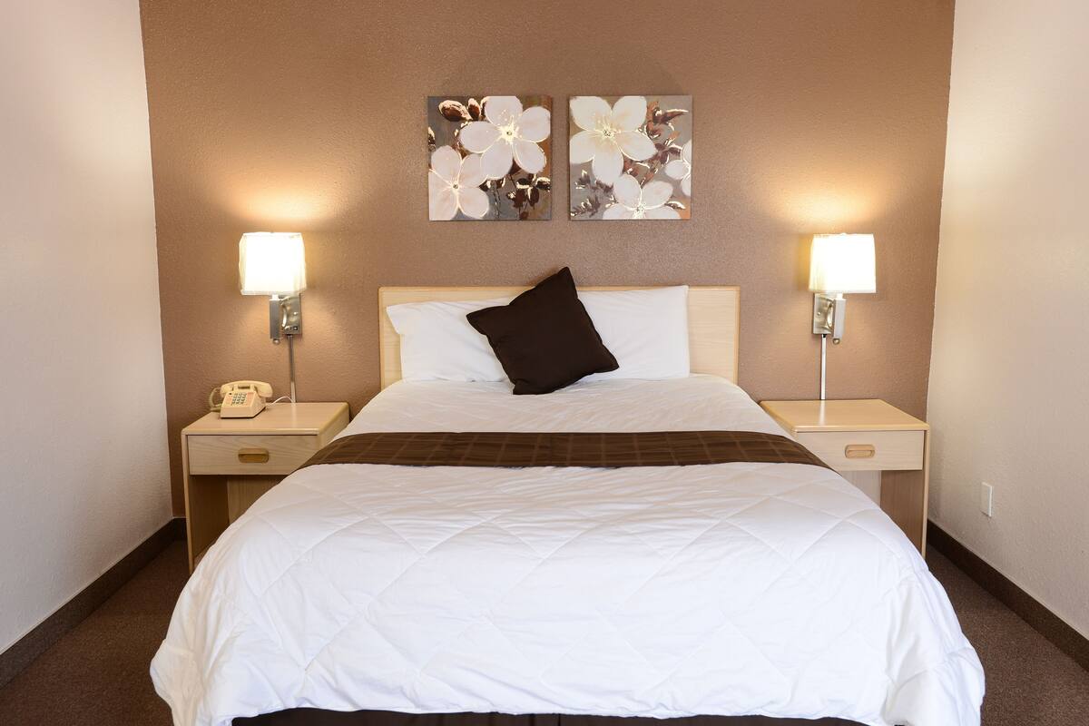 A hotel room with a large bed, two bedside tables, a telephone, and wall-mounted lamps.