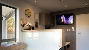 A modern kitchen with a large window, a clock, and a flat-screen TV mounted on the wall.