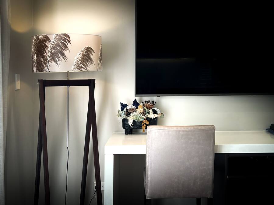 Una habitación moderna con un escritorio, una silla, una lámpara con pantallas de plumas y un televisor de pantalla plana montado en la pared.