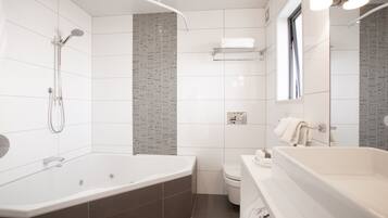 Een moderne badkamer met een ruime badkuip, een aparte douche, toilet en wastafel.