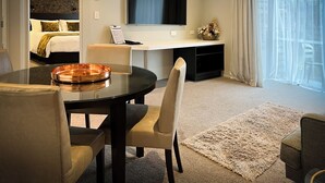 A modern hotel room with a bed, a desk, a TV, and a dining area with chairs and a table.