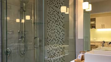 Une salle de bain moderne avec une douche à parois de verre, un mur recouvert de carreaux et un lavabo blanc agrémenté d’un plateau en bois.