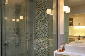 A modern bathroom with a glass-enclosed shower, a tiled backsplash, and a white sink with a wooden tray.